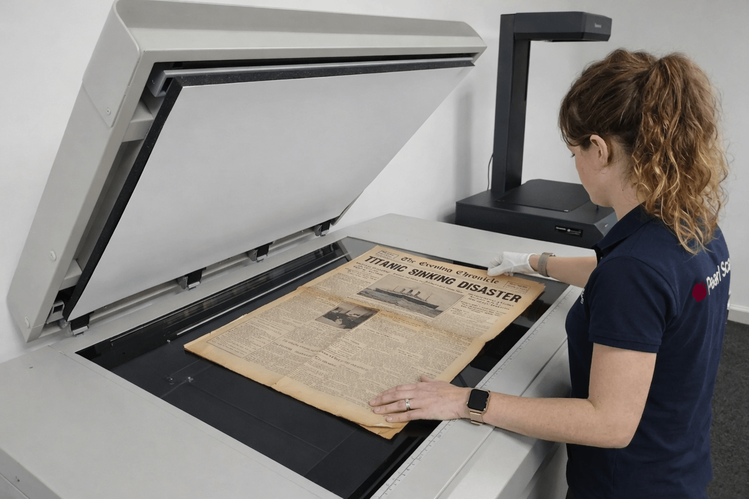 “Technician scanning oversized newspapers on a large format flatbed scanner for digital archiving”