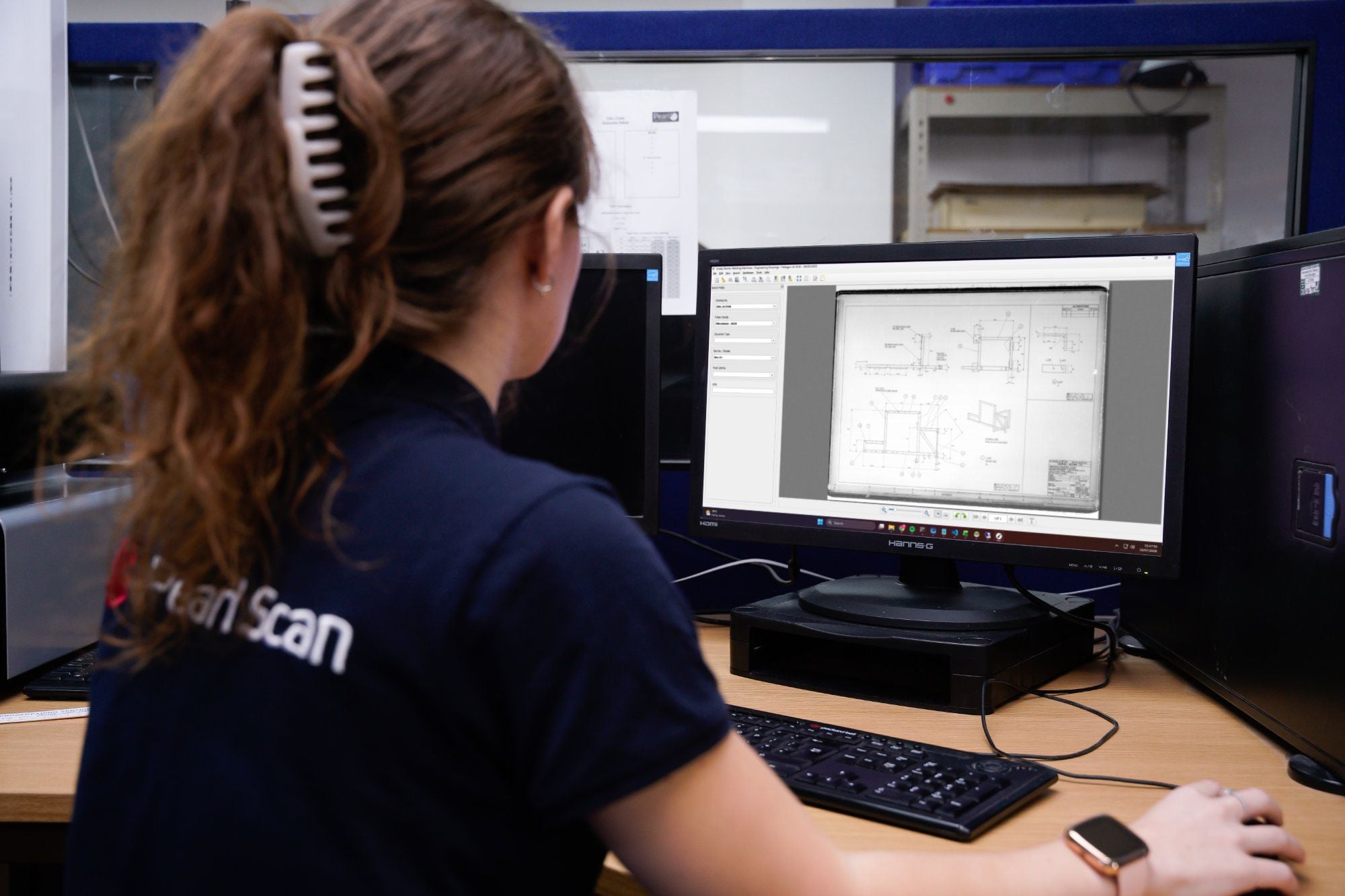scanning operator wearing pearl scan uniform, sitting in front of the PC monitor and looking at the PC monitor screen which has an image of a drawing and indexing application.